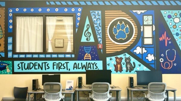 Bright wall mural including GCC and library specific graphics such as a cougar paw, academic program graphics such as skeletons, medical equipment, and GCC tartan for our fashion program, and text that says "Students first, always"